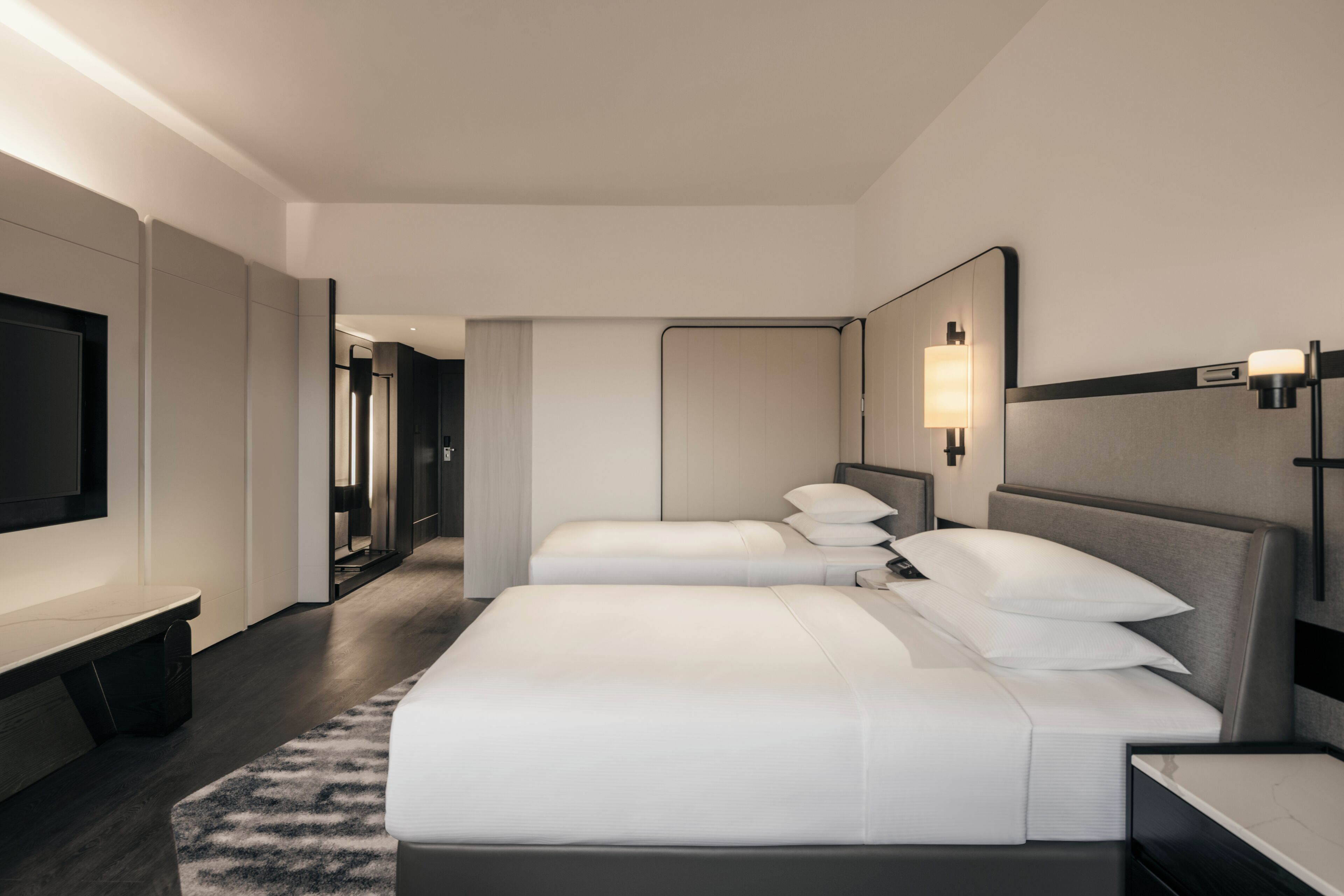 A modern hotel room with two beds, a flat-screen TV, and a large mirror.