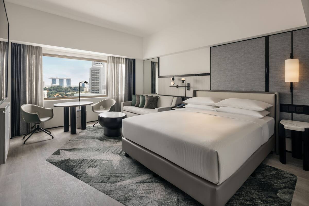 Habitación de hotel moderna con una cama grande, un escritorio y una silla. Se ve un paisaje urbano a través de la ventana.