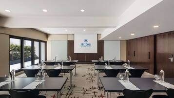 A conference room with tables, chairs, and a projector screen displaying the Hilton logo.