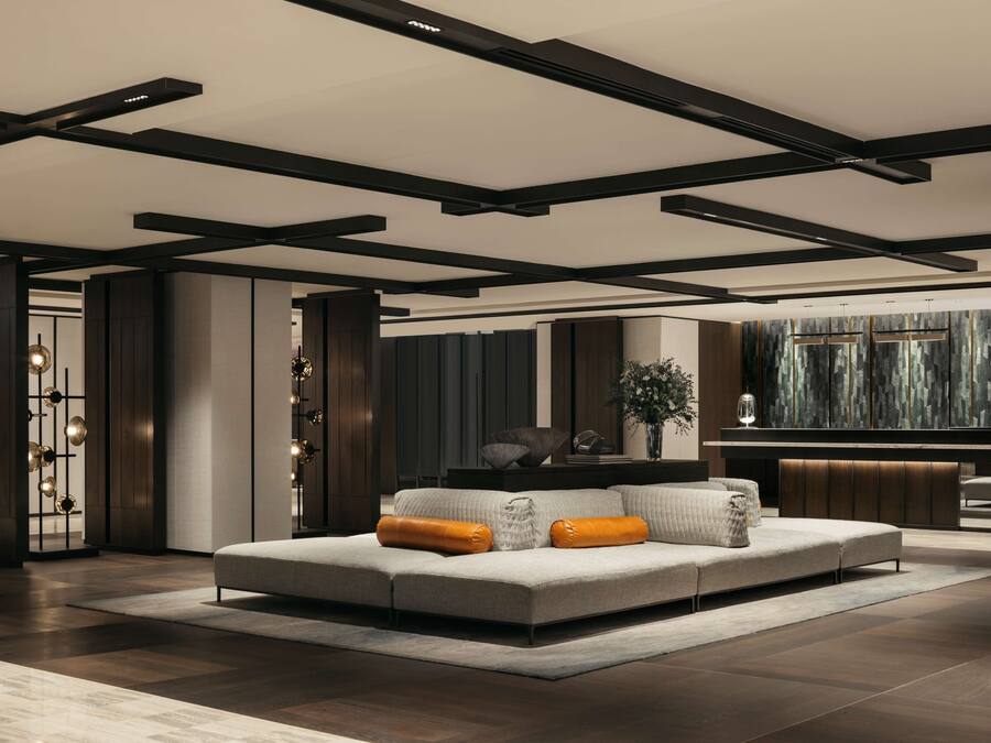 A modern living room with a sectional sofa, dark wooden flooring, and a minimalist ceiling design.