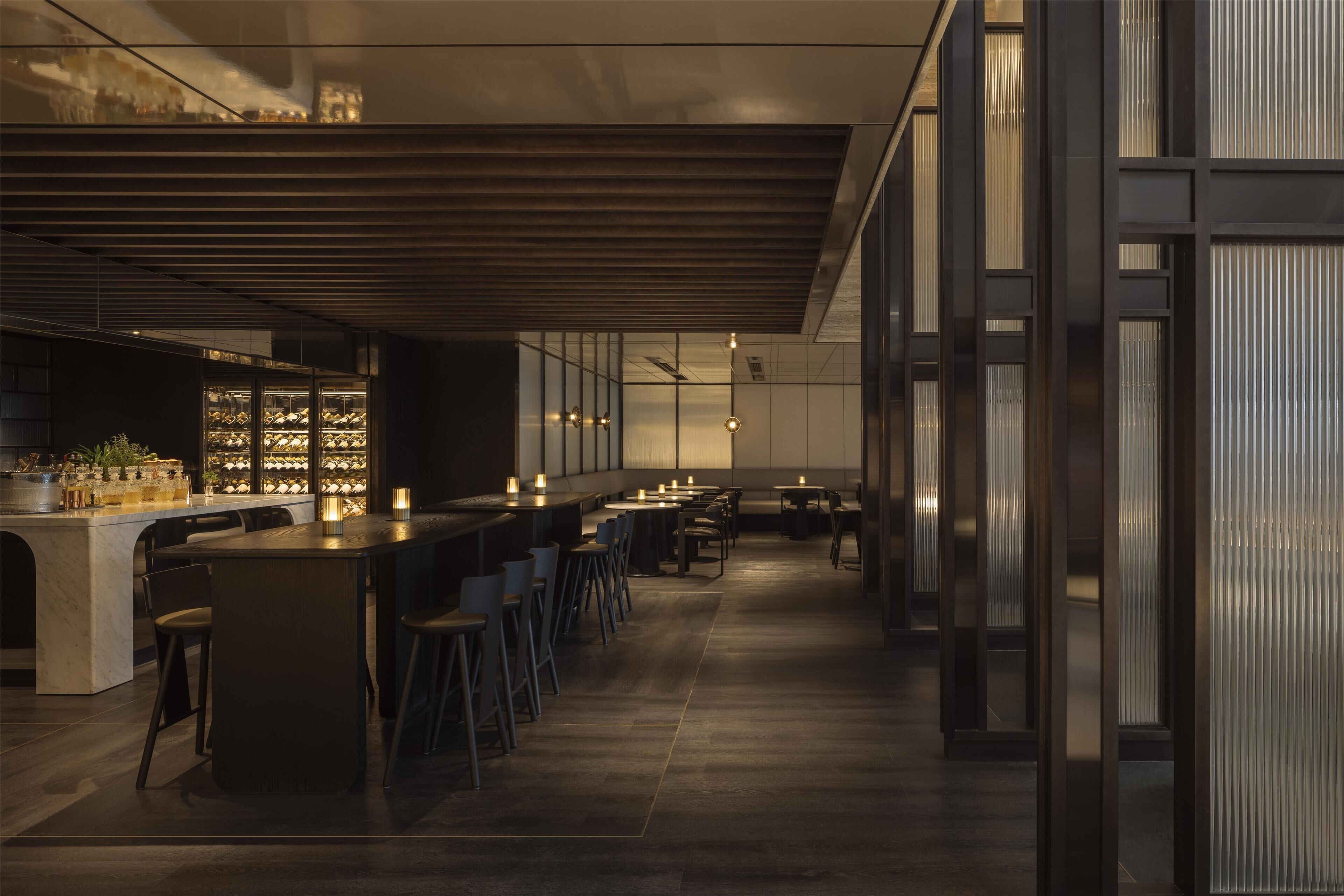 Zona de bar moderna con una barra alargada, taburetes y una selección de vinos.
