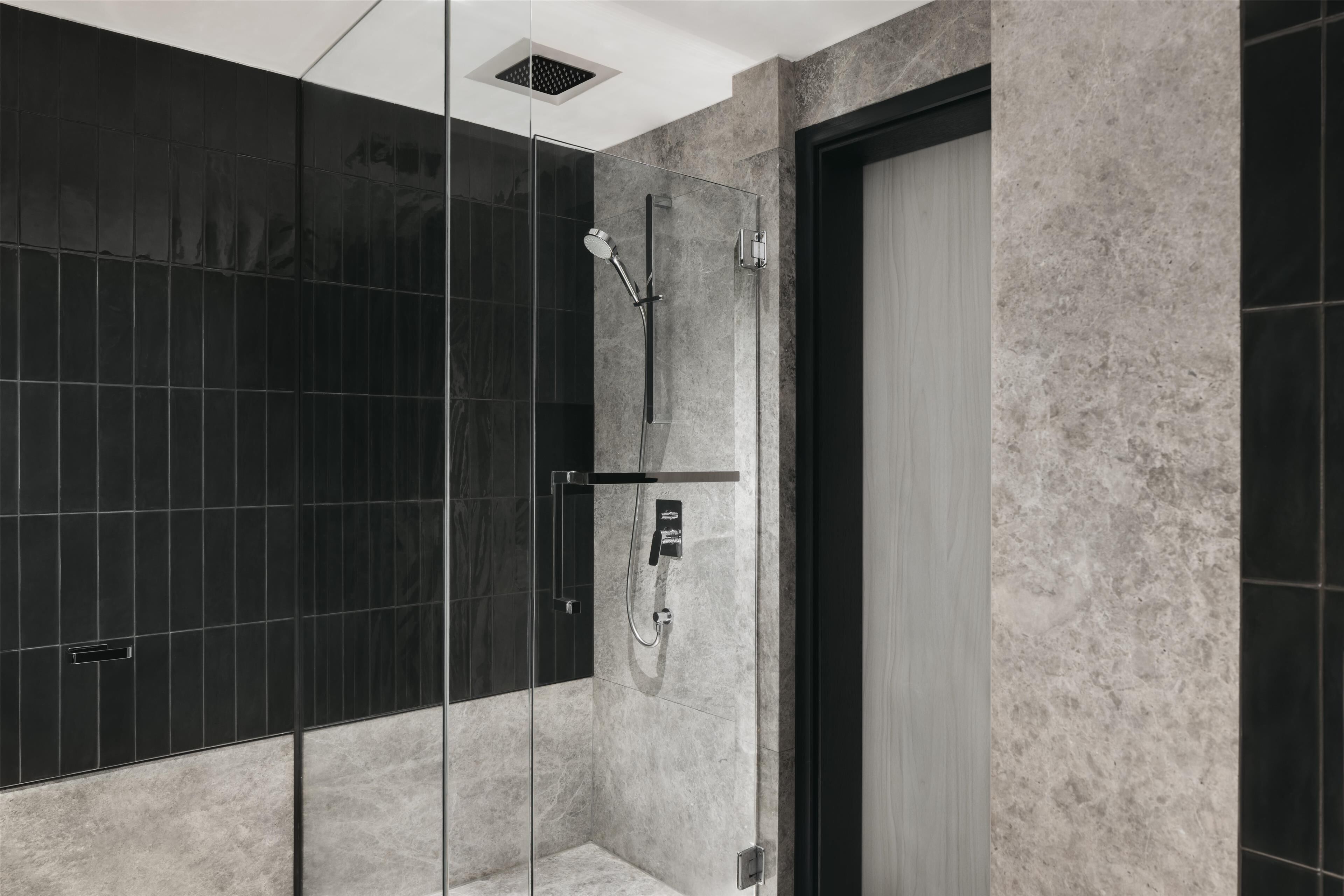 Un baño moderno con cabina de ducha de vidrio, pared revestida de baldosas negras y suelo de mármol.