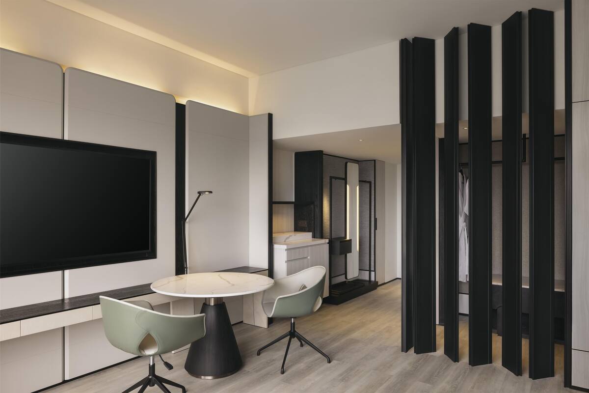 Una habitación de hotel moderna con una televisión de pantalla plana, una mesa de comedor redonda, dos sillas, un armario y un espejo.