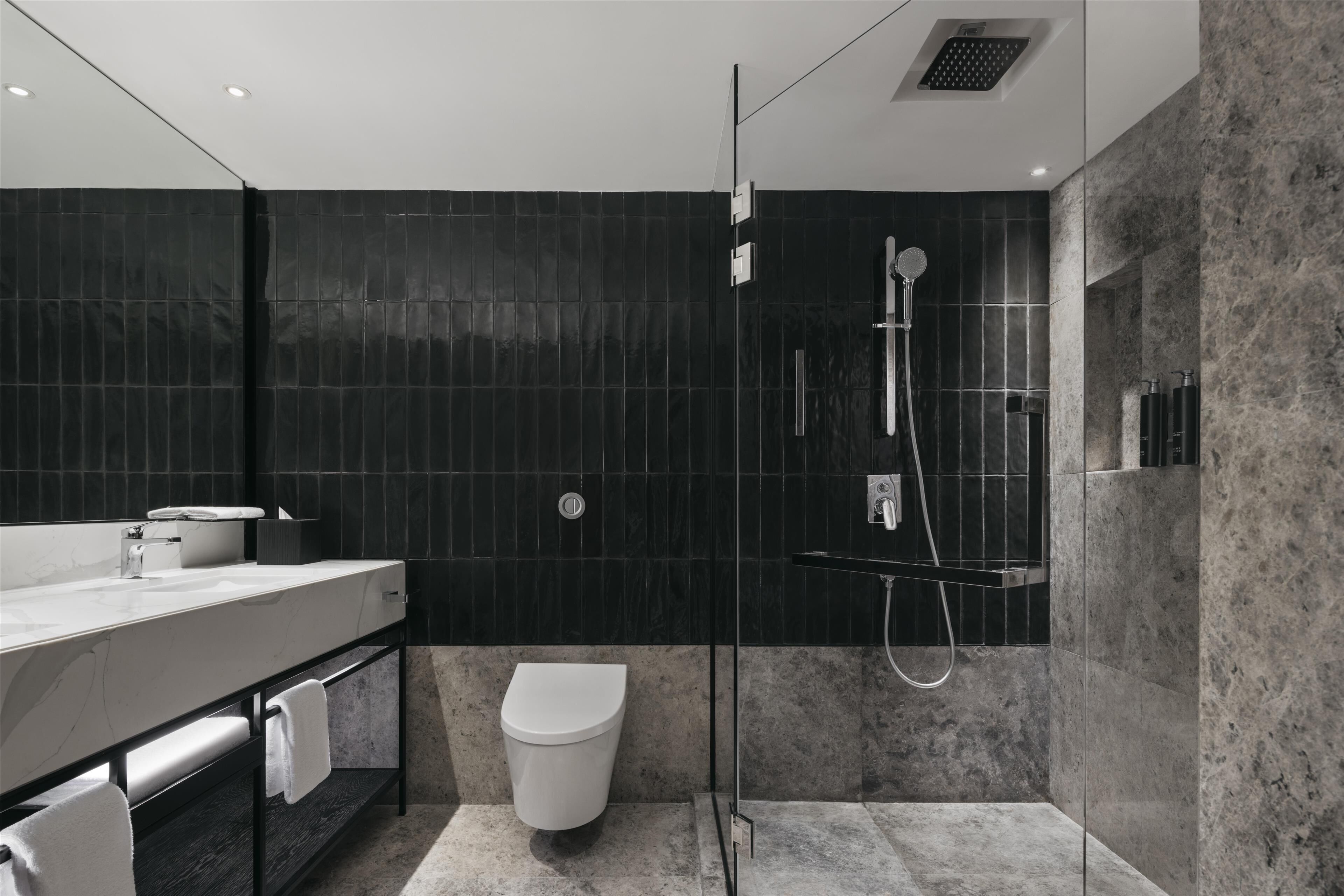 A modern bathroom with a marble sink, a toilet, and a glass-enclosed shower area.