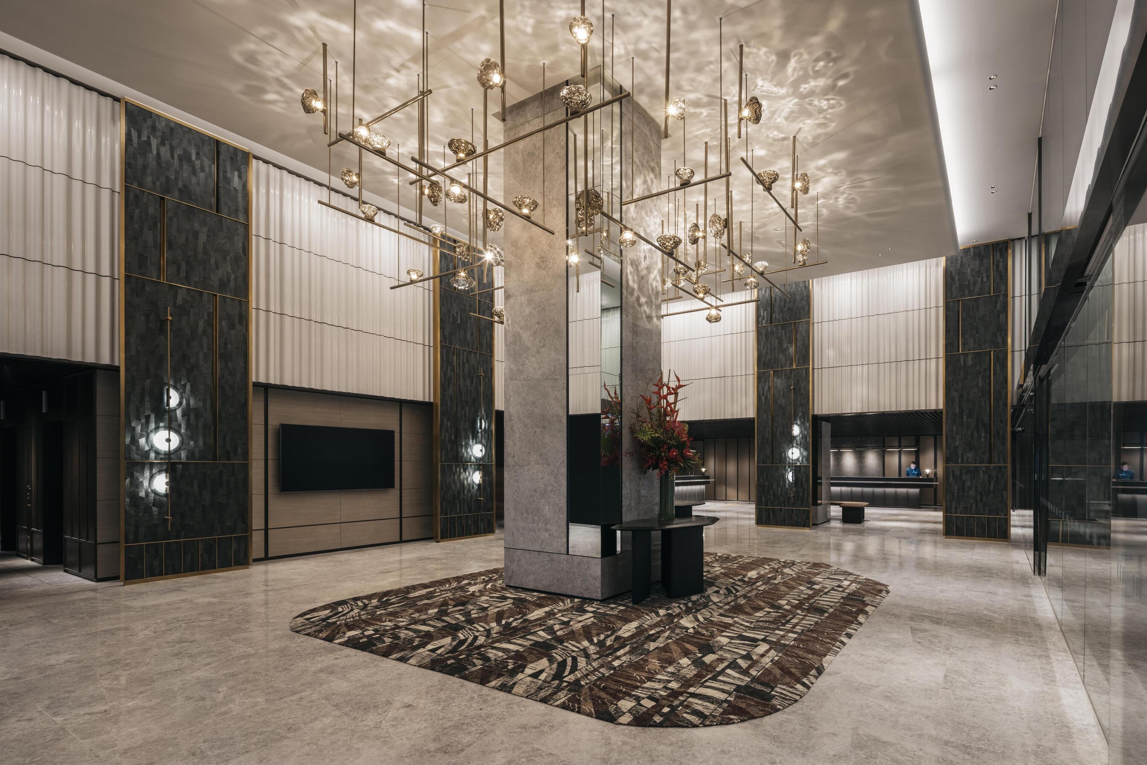 A spacious lobby with a modern chandelier, a central pillar, and a patterned rug.