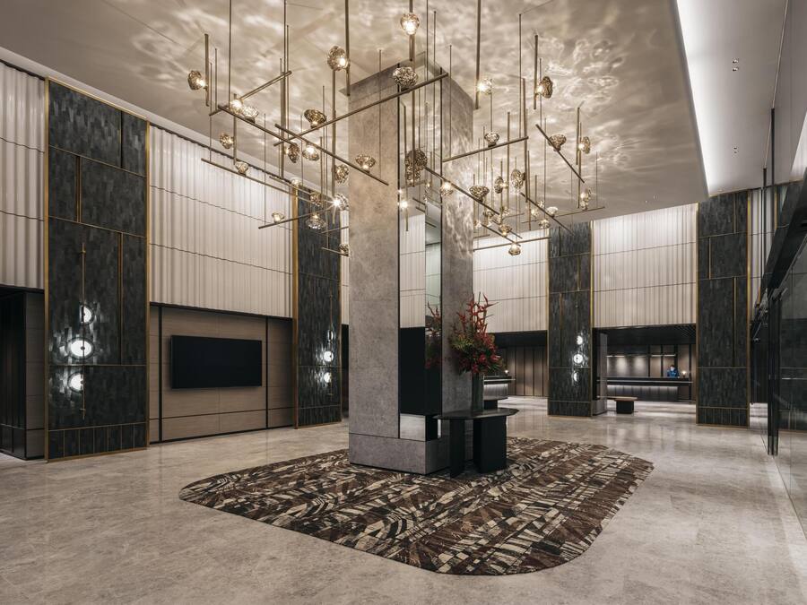 A spacious lobby with a modern chandelier, a central pillar, and a patterned rug.