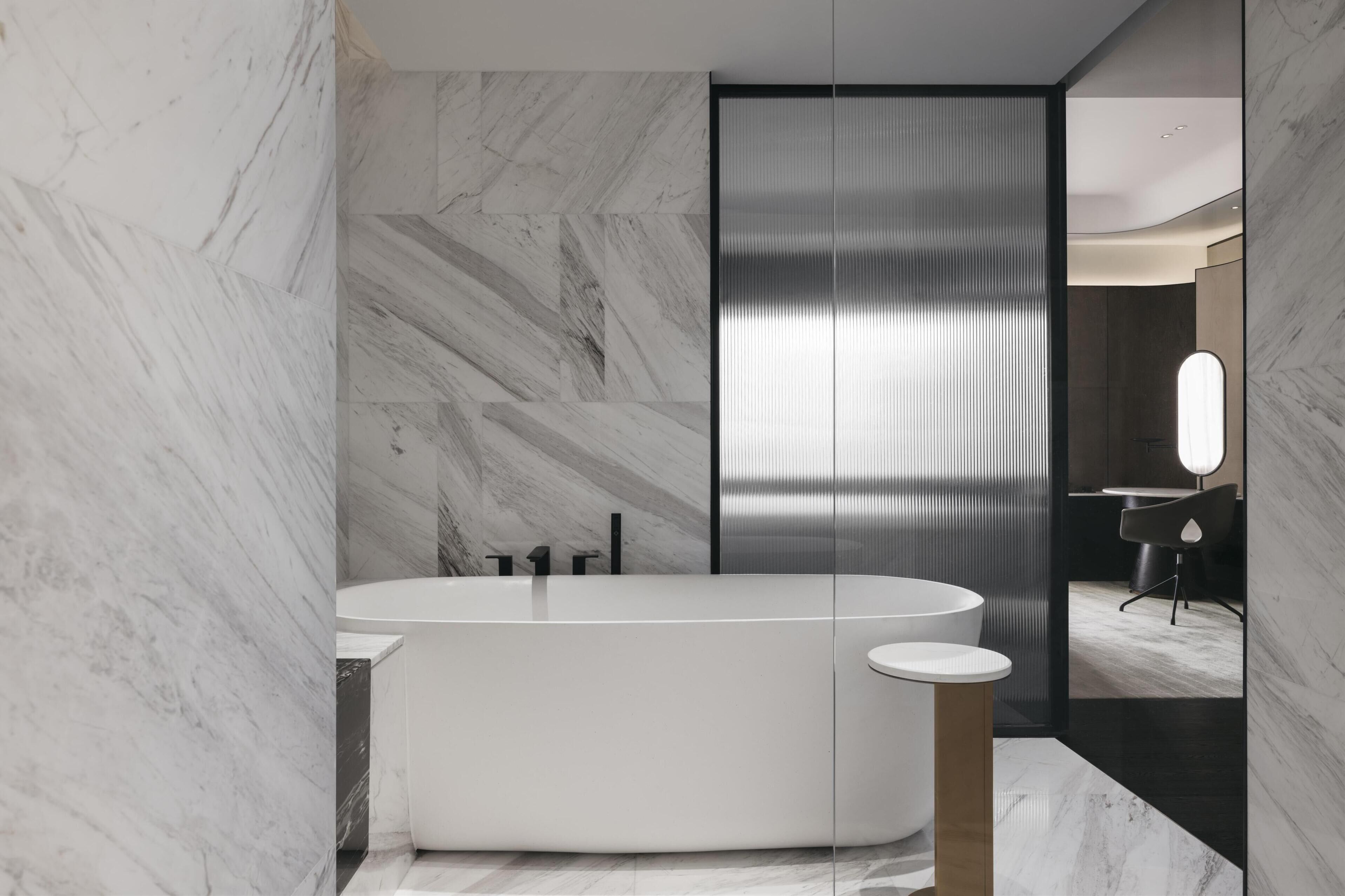 Un baño moderno con una bañera independiente, paredes de mármol y un espejo grande.