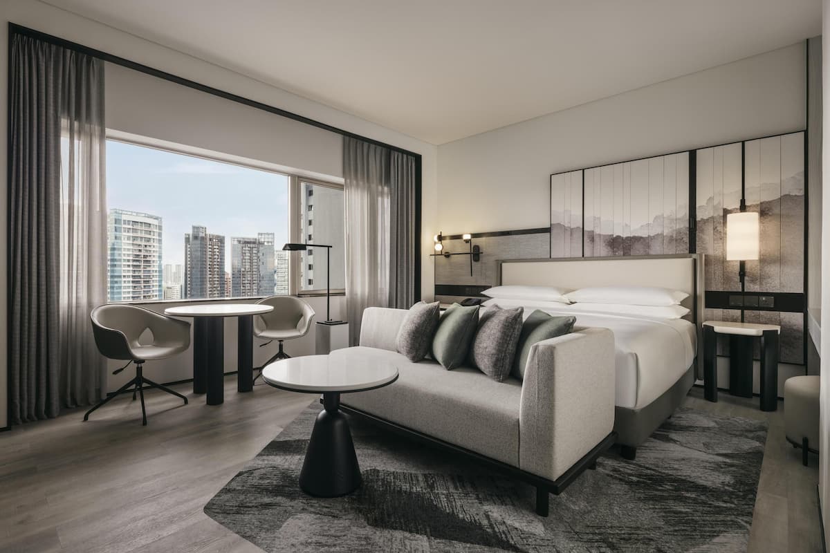 Habitación de hotel moderna con una cama grande, un sofá, una mesa de comedor y vistas a la ciudad.
