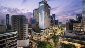 Un hotel moderno con un llamativo letrero de Hilton, rodeado de edificios altos y una concurrida calle urbana al anochecer.