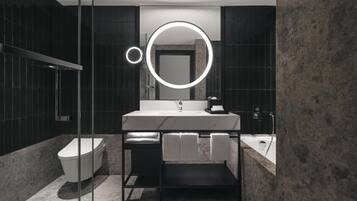 Un baño moderno con un espejo redondo, lavabo blanco y una bañera.