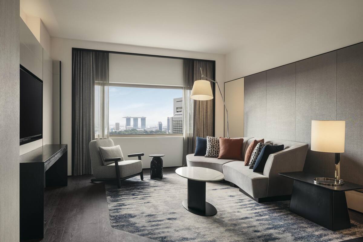 Una habitación de hotel moderna con un ventanal grande, un televisor de pantalla plana, un sofá, una mesita de café y una lámpara.