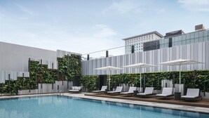 Un área de piscina moderna al aire libre con sillones de descanso y sombrillas, rodeada por un jardín vertical y una fachada de edificio contemporánea.
