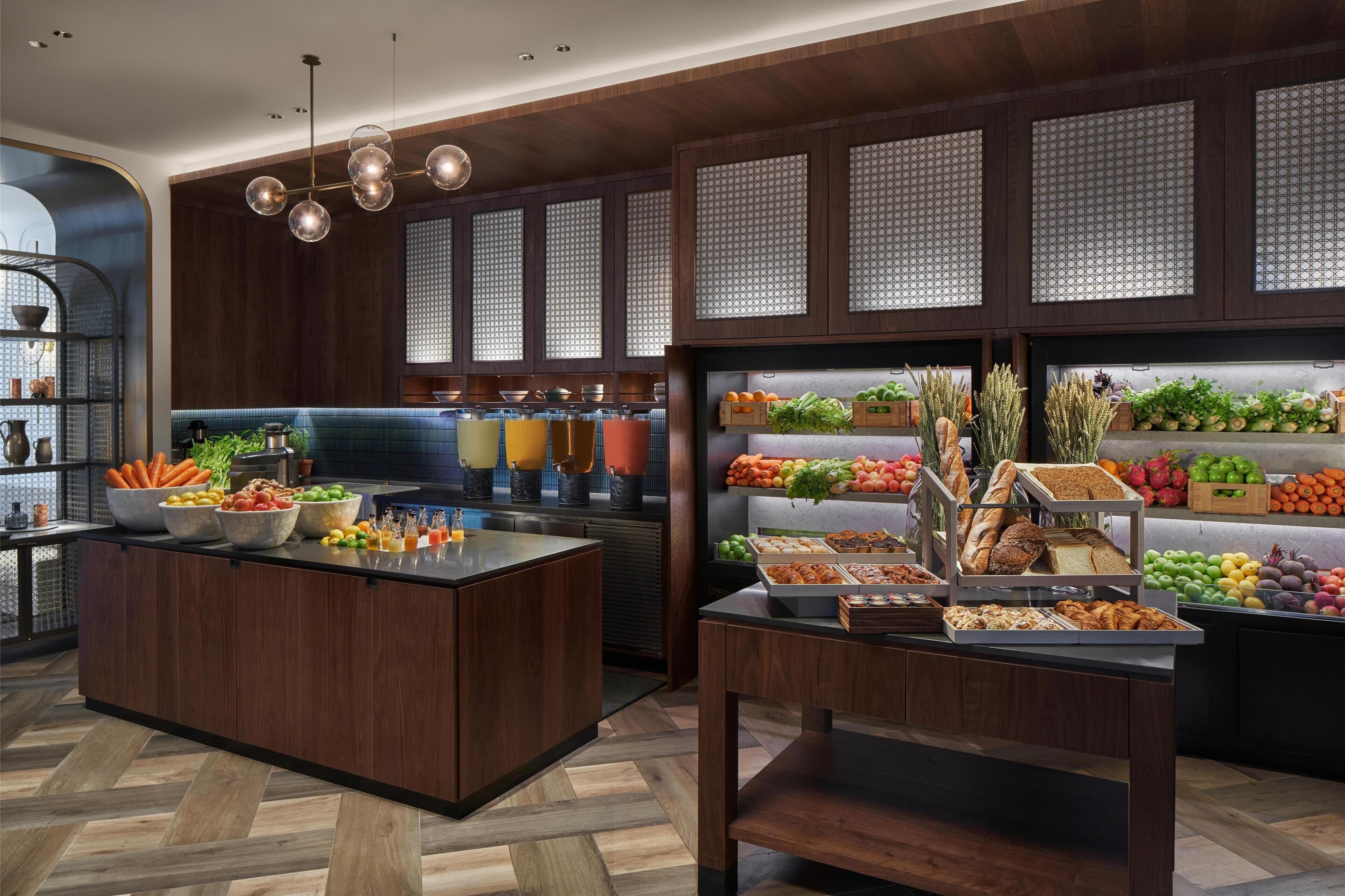 Una cocina moderna con armarios de madera, una isla central con cuencos de frutas y verduras, y una vitrina con diferentes productos alimenticios.
