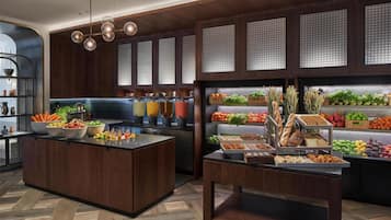 Una cocina moderna con armarios de madera, una isla central con cuencos de frutas y verduras, y una vitrina con diferentes productos alimenticios.