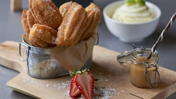 Churros en un vaso de metal, un tazón de crema batida y un frasco de dulce de leche sobre una tabla de madera.