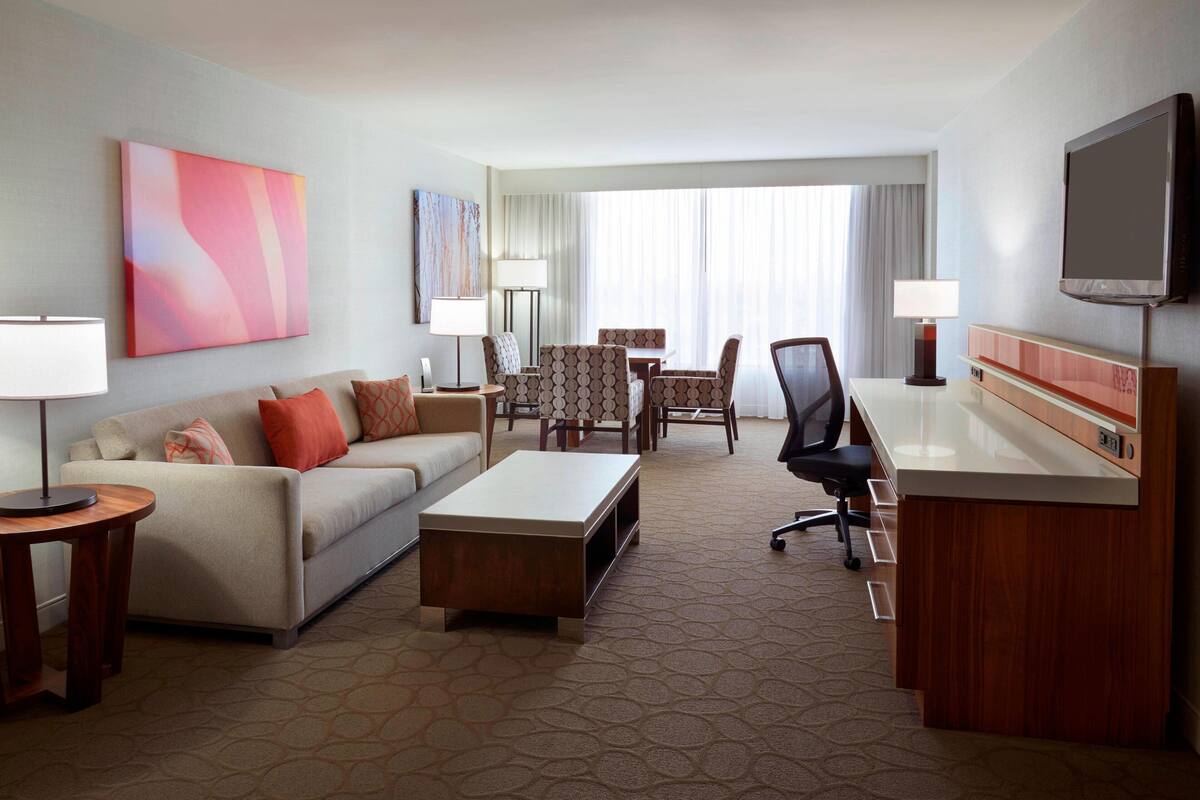 A hotel room with a sofa, coffee table, TV, desk, and chairs.