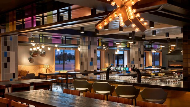 Un intérieur de restaurant moderne, avec un bar, des espaces de repos et un grand luminaire décoratif.