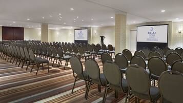 Un salón de conferencias con hileras de sillas, piso alfombrado y dos pantallas mostrando el logotipo de Delta Hotels.
