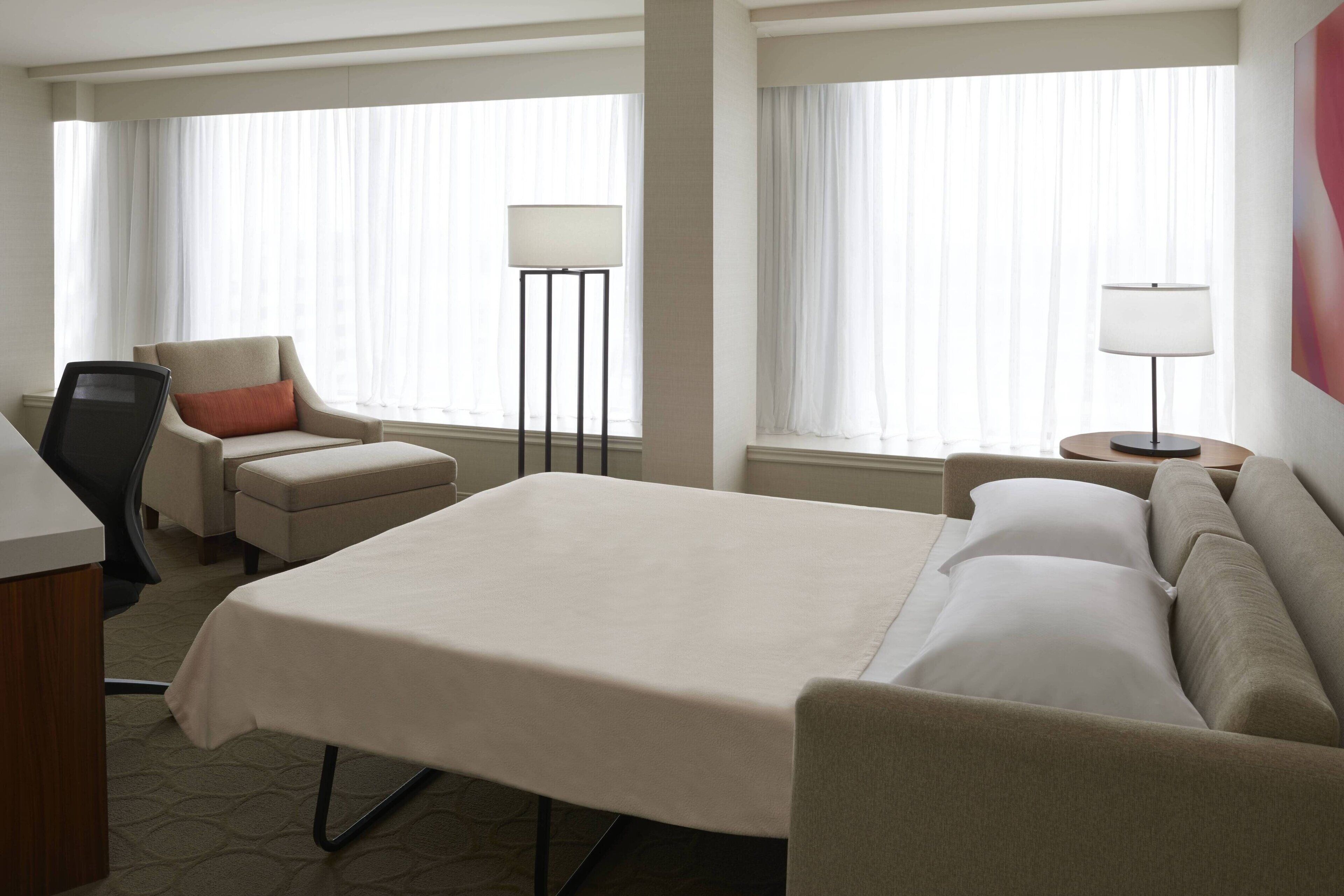 A hotel room with a large bed, a desk, a chair, a sofa, and two lamps.