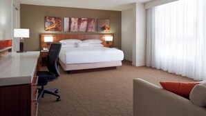 Une chambre d’hôtel avec un lit, un bureau, une chaise et une grande fenêtre avec des rideaux.