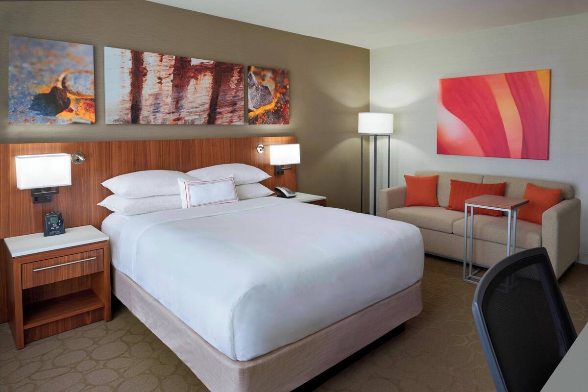 A hotel room with a large bed, two bedside tables with lamps, a sofa, and artwork on the walls.
