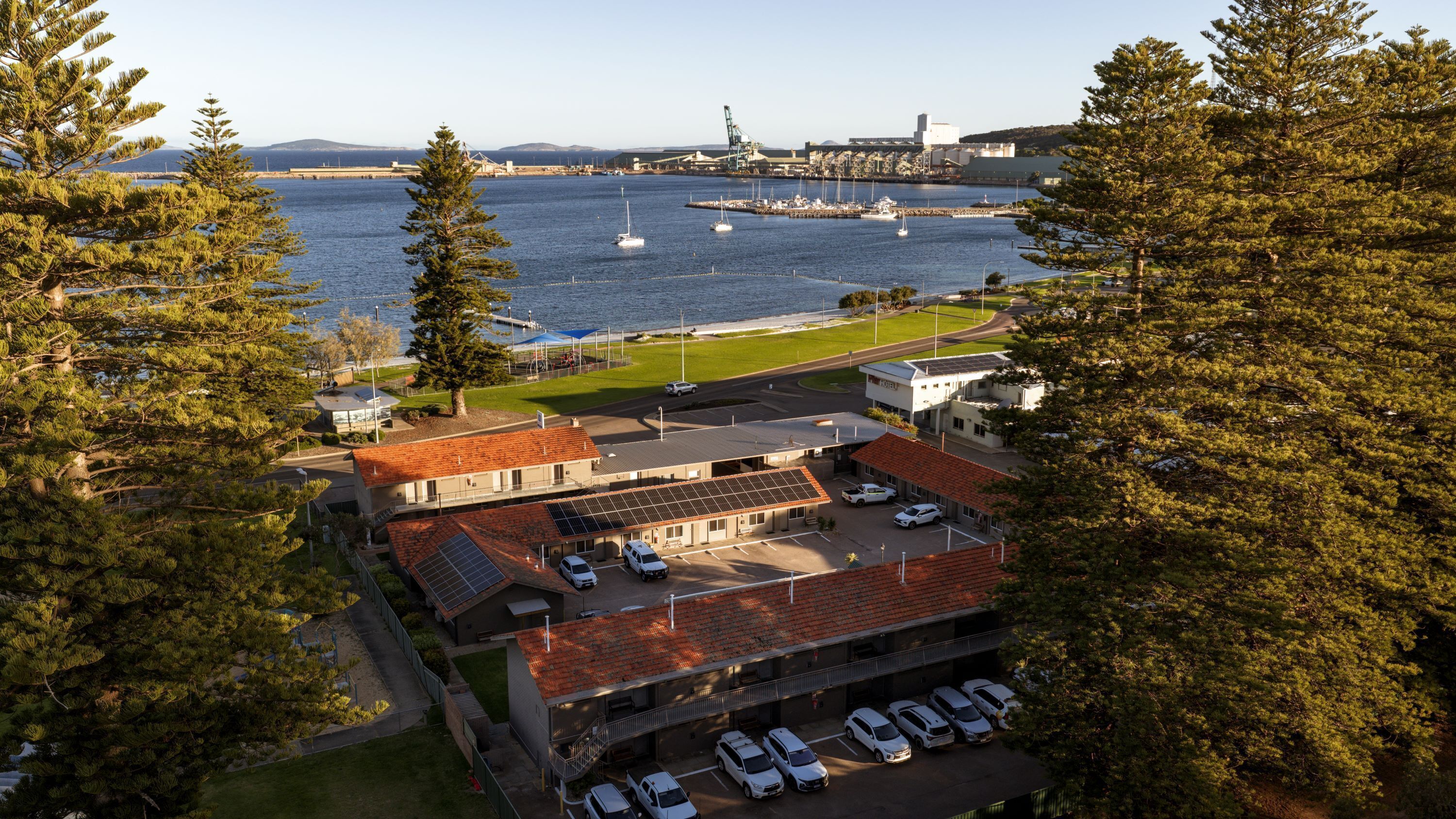 Un hôtel situé sur la côte, doté d’un parking, d’un bâtiment équipé de panneaux solaires et offrant une vue sur la mer et le port.