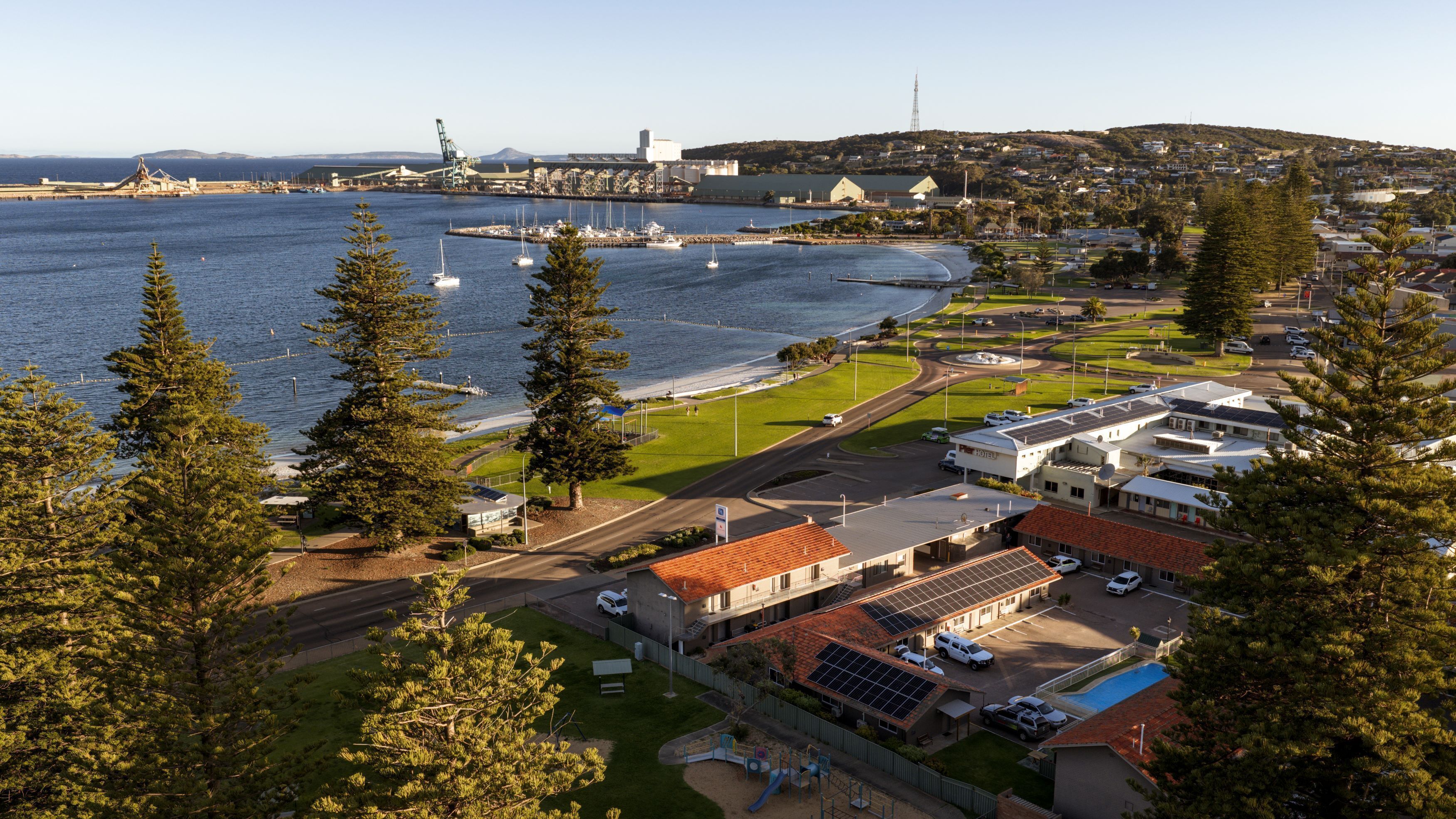 A coastal hotel with a view of the sea, a playground, and a parking area.