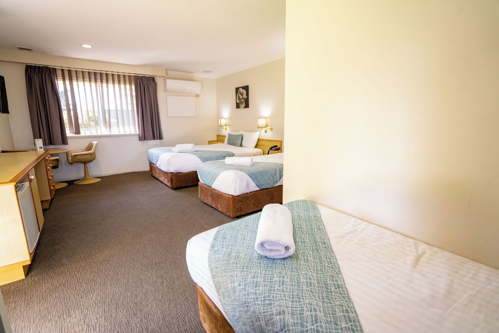 A hotel room with two beds, a desk, a chair, and a window with curtains.
