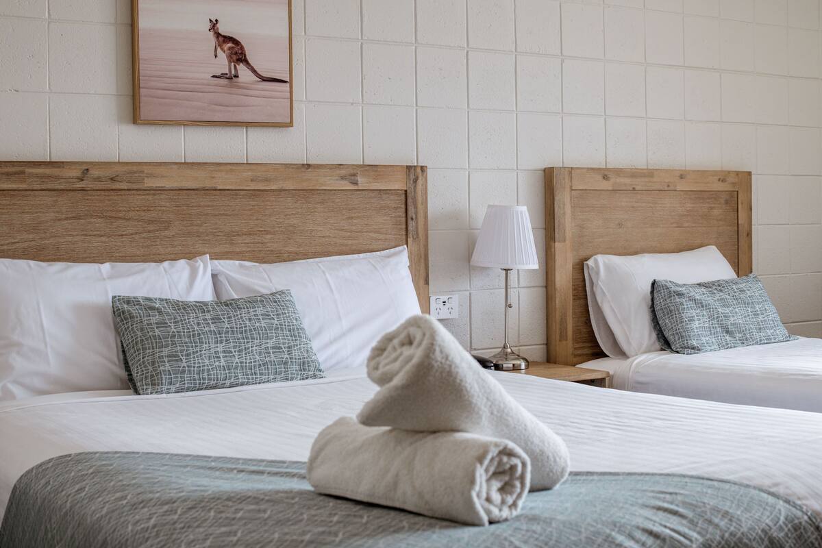 A hotel room with two beds, each with white linens and a wooden headboard. There is a framed picture of a kangaroo on the wall above the beds.