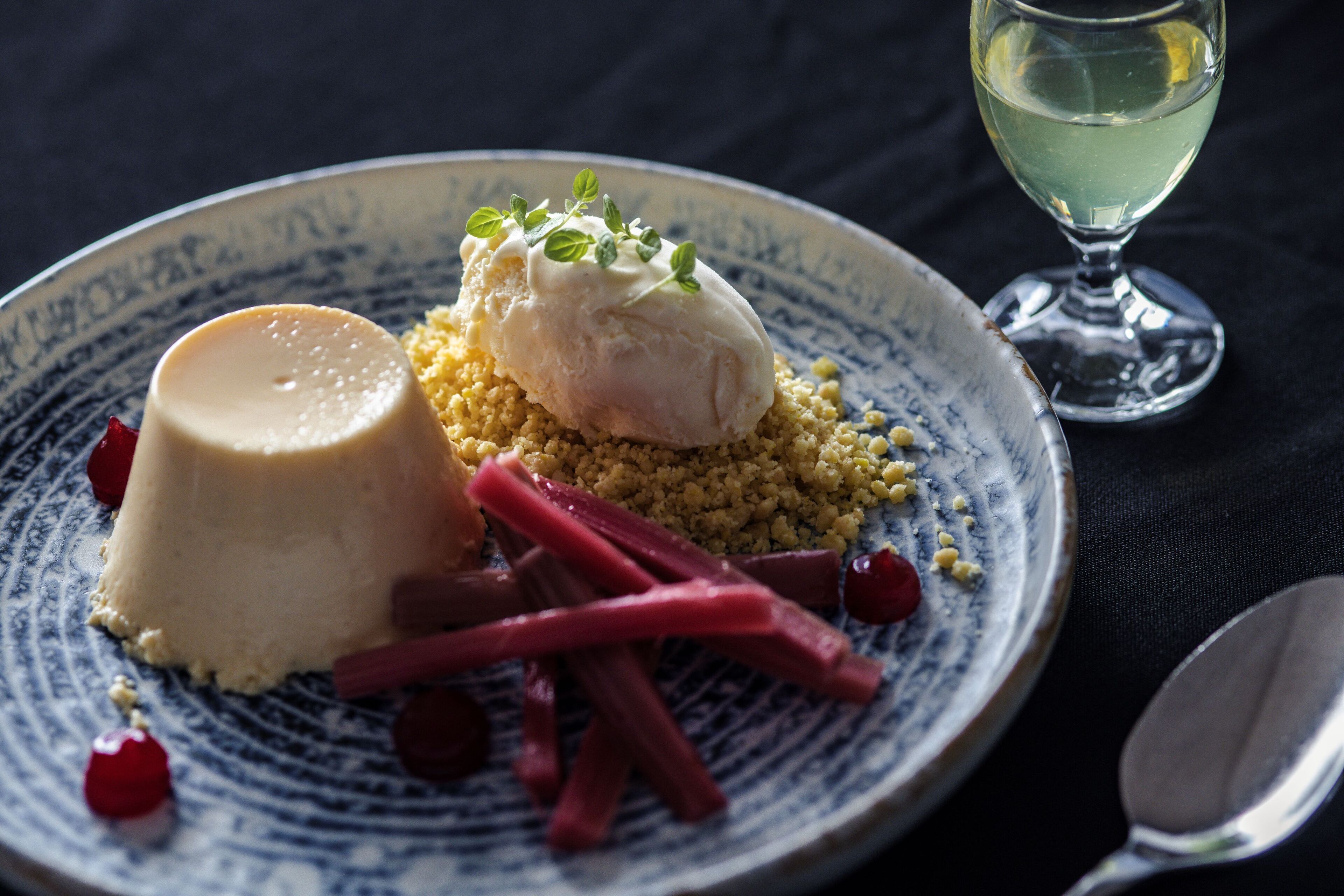Een dessertborden met panna cotta en een bolletje ijs, versierd met kruiden, geserveerd op een blauw-wit bord.