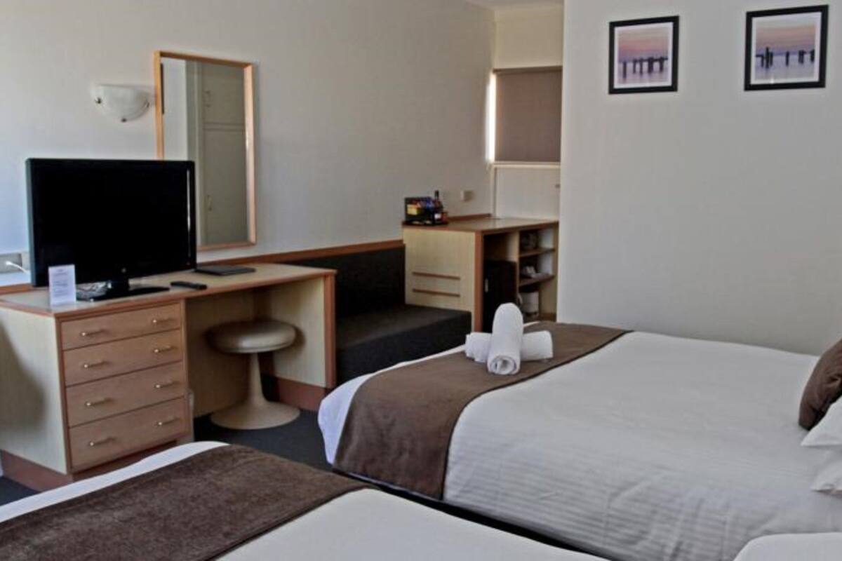 A hotel room with two beds, a desk with a chair, a television, a wardrobe, and two framed pictures on the wall.