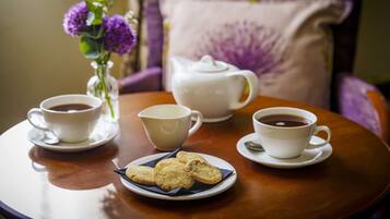 A round wooden table with two white cups of coffee, a white teapot, and a plate with cookies.