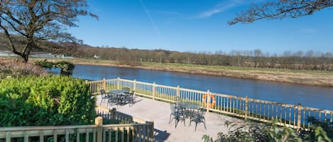 A riverside patio with outdoor seating and a wooden fence.