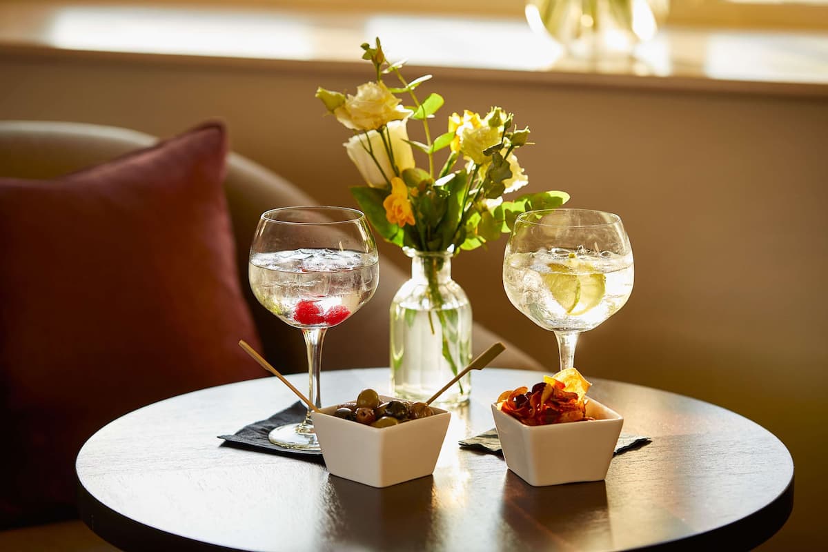 Una mesa redonda con dos vasos de agua, un pequeño jarrón con flores y dos recipientes pequeños con aperitivos.