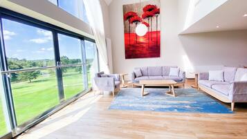 A spacious living room with a large window, a modern sofa set, and a painting of red trees.