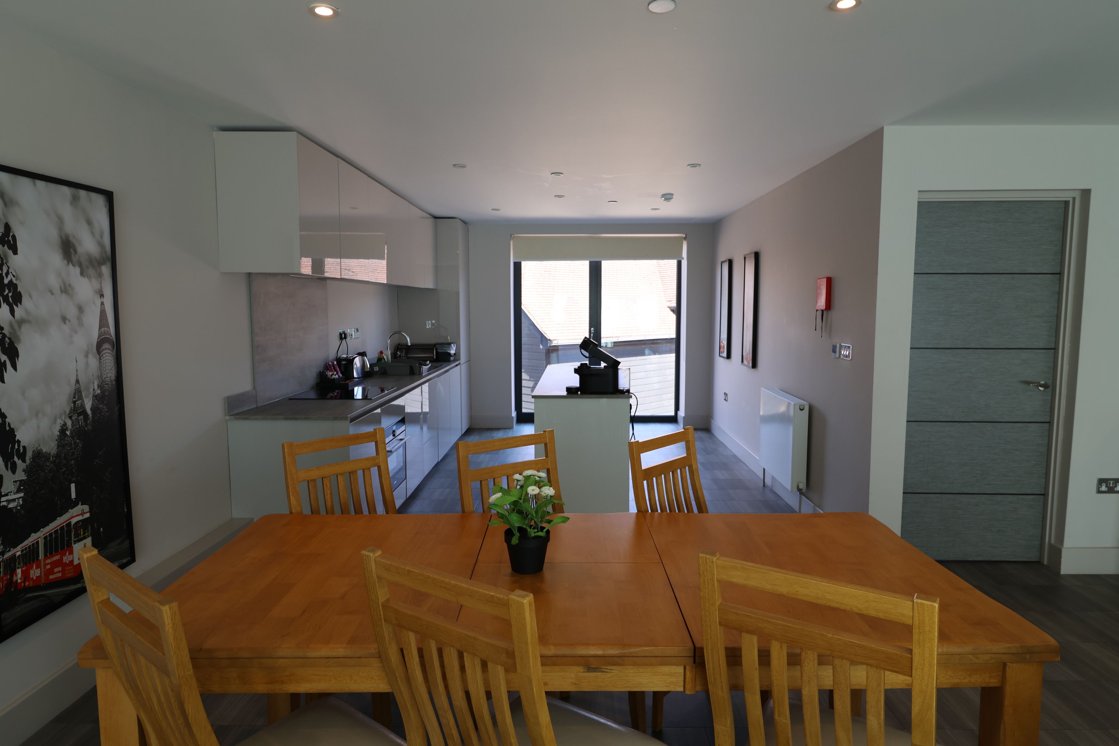 A modern kitchen with white cabinets, a dining table with chairs, and a large window.