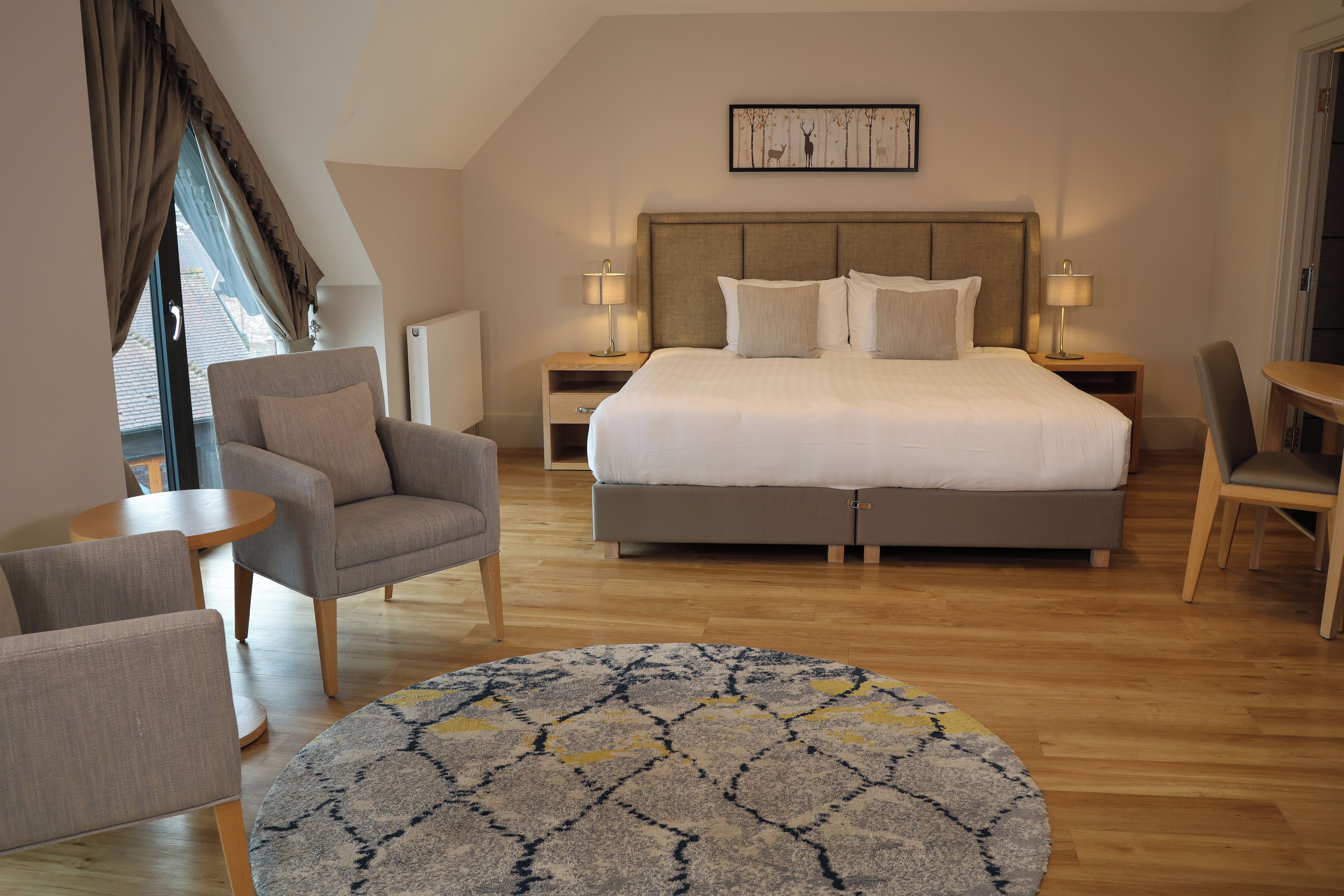 A hotel room with a bed, two bedside tables, a chair, a round rug, and a window with curtains.