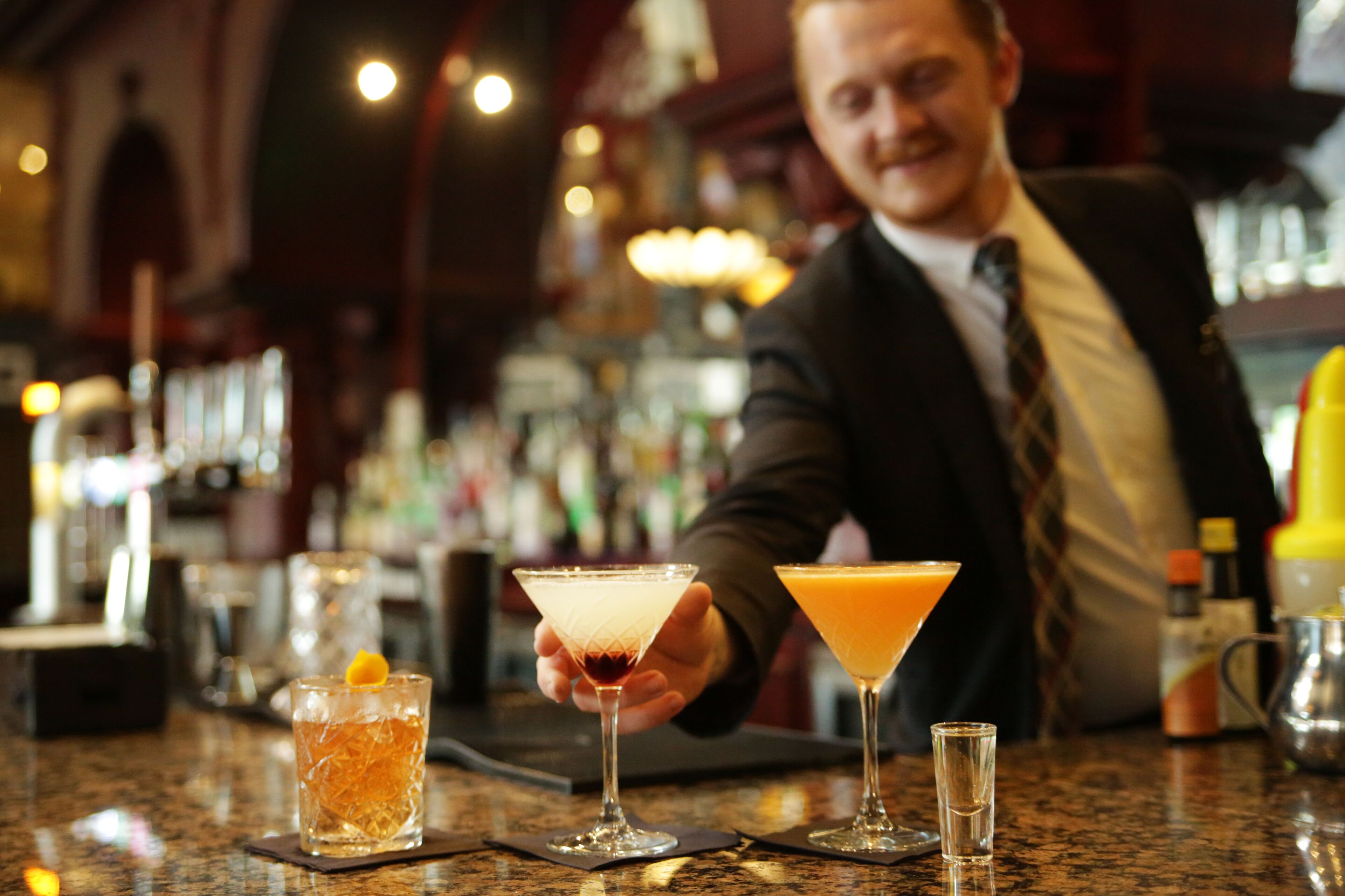 Een bar met een barman die een cocktail vasthoudt, een martini glas en een highball glas op een granieten aanrecht.