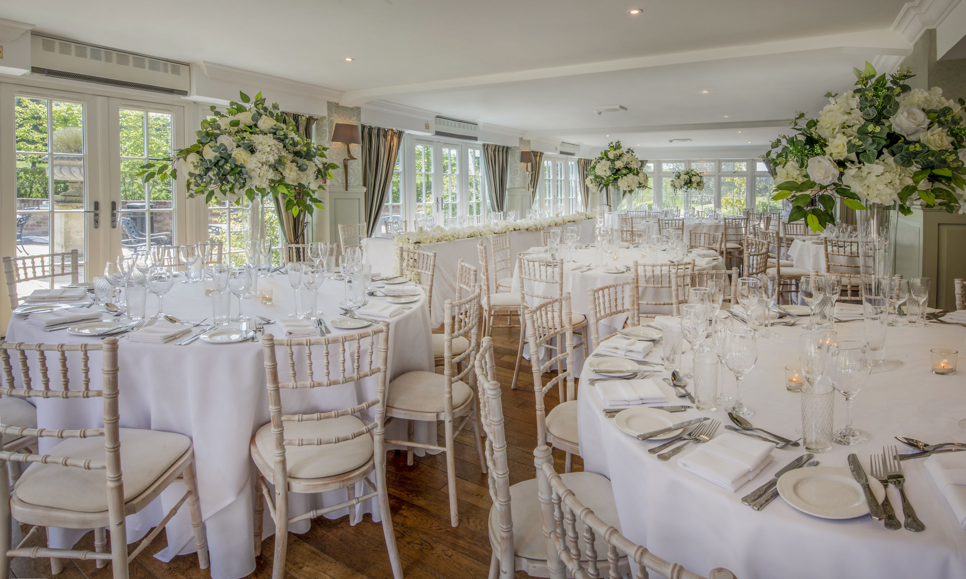A banquet hall with round tables set for dining, white chairs, and floral centerpieces.