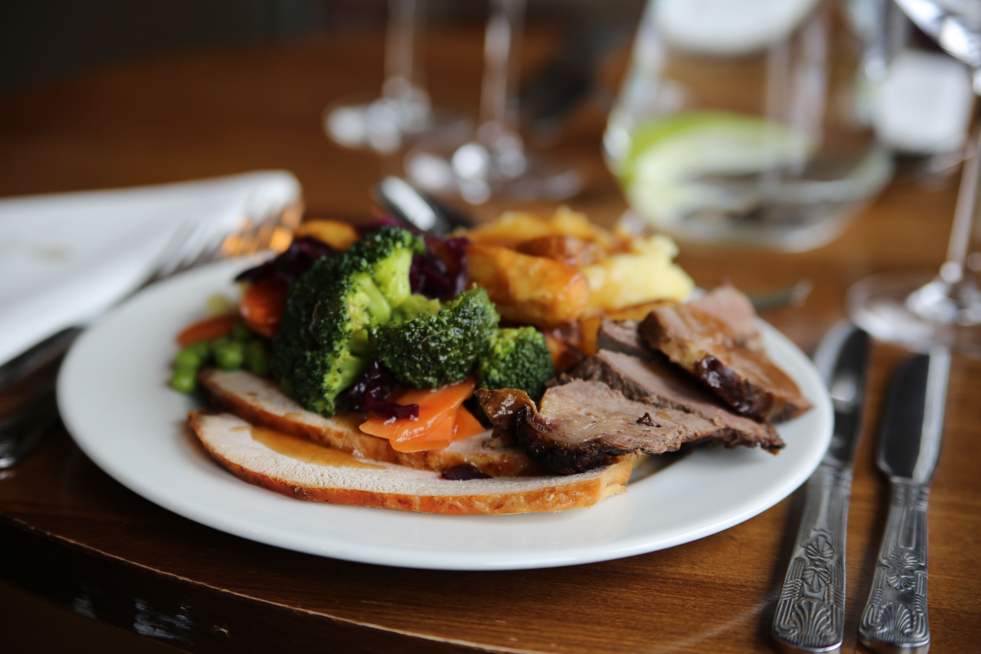 Un plato de comida con pan, carne y verduras sobre una mesa de madera.