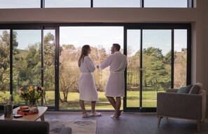 A couple in matching robes standing by a large window overlooking a garden. - Old Thorns Golf Resort and Spa Hampshire by Accor (Liphook)