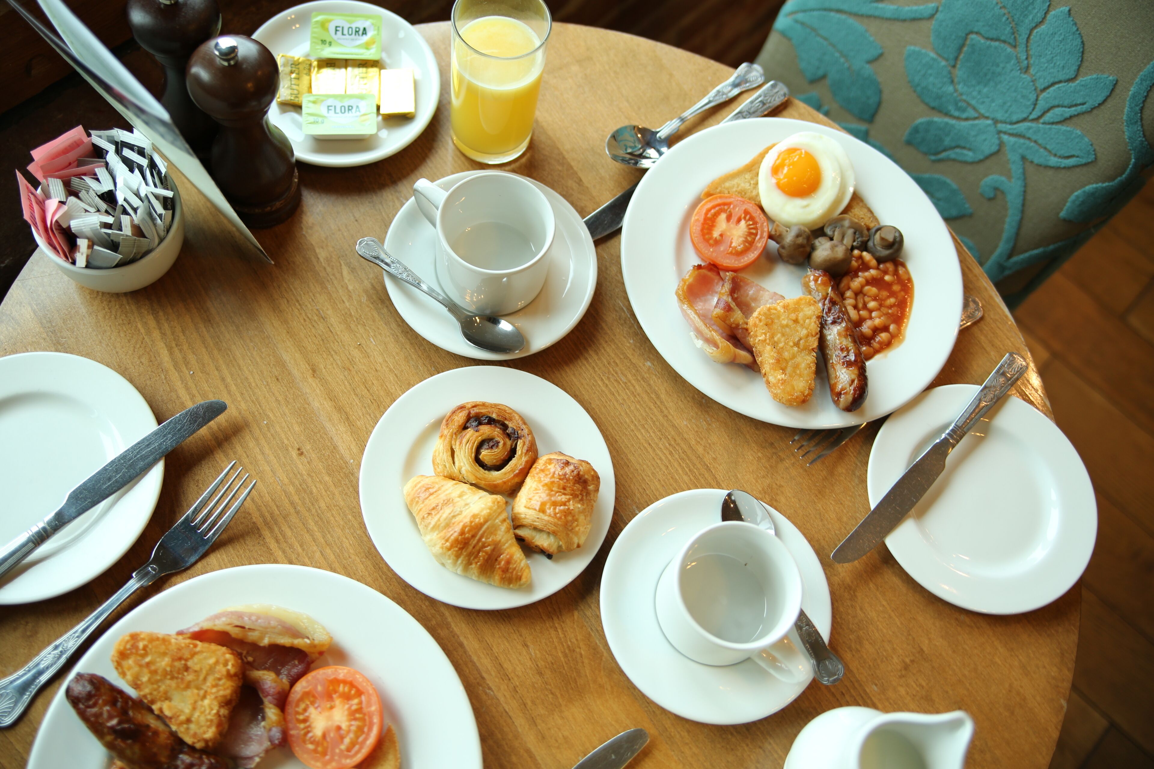 A breakfast table with plates of food, utensils, and a glass of orange juice.
