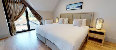 A modern bedroom with a large bed, two bedside tables with lamps, a painting on the wall, and a view through the window.