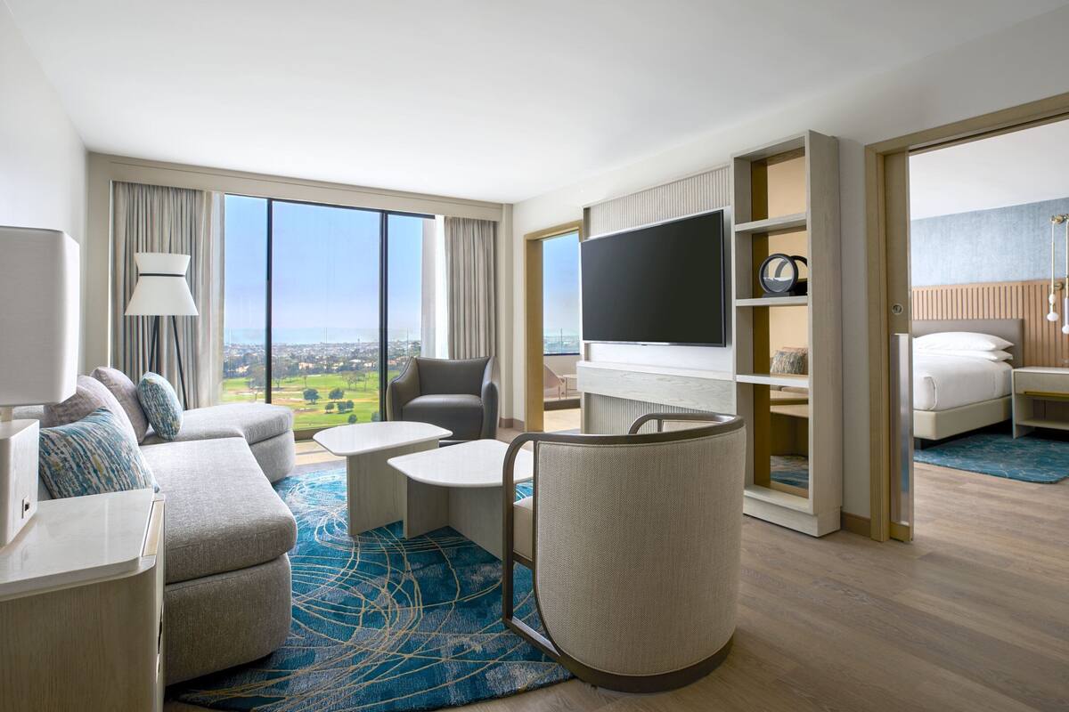 Una habitación de hotel moderna con un ventanal grande, un sofá, un televisor, un escritorio y una cama.