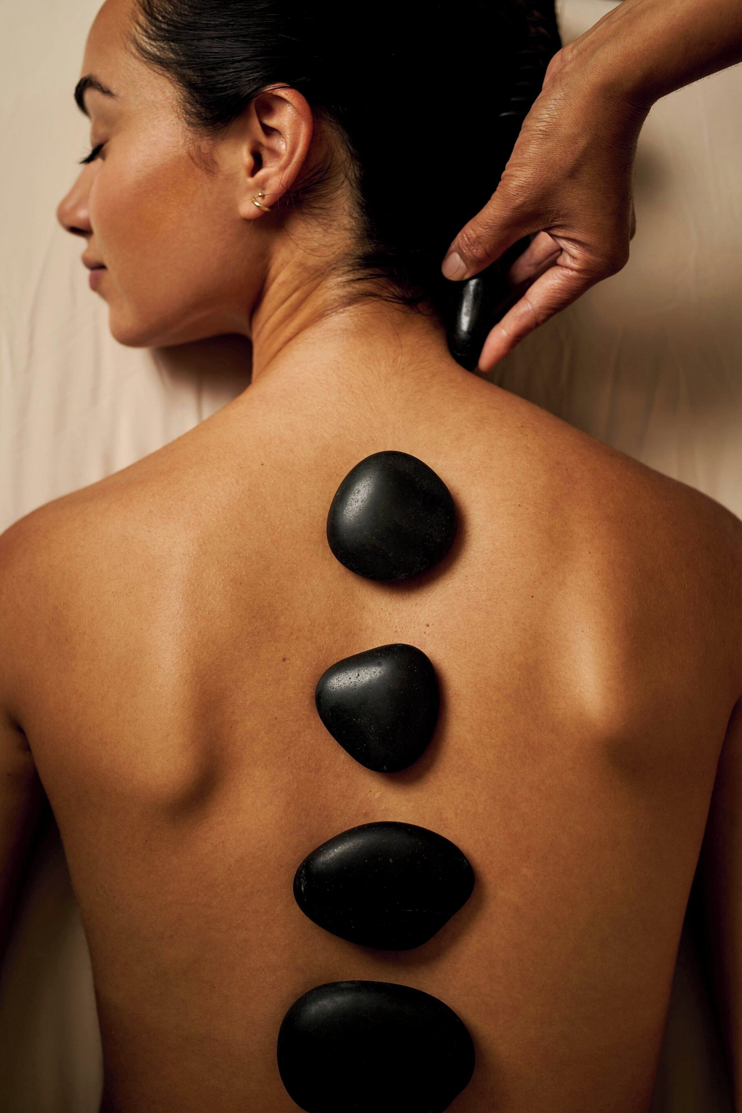 Eine Person erhält eine Rückenmassage mit schwarzen Steinen, die entlang der Wirbelsäule platziert sind.