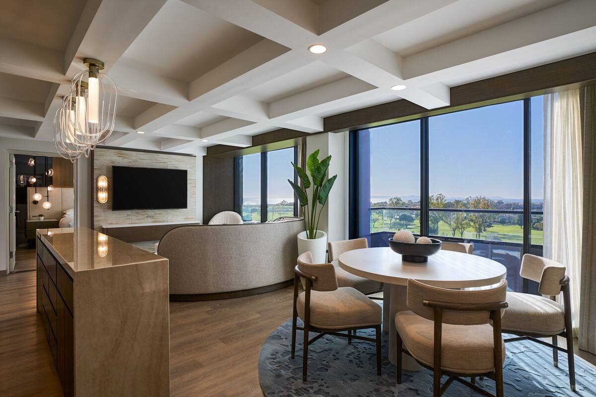 Una cocina moderna con una isla central, un comedor con una mesa redonda y sillas, y ventanas amplias que ofrecen vistas al exterior.