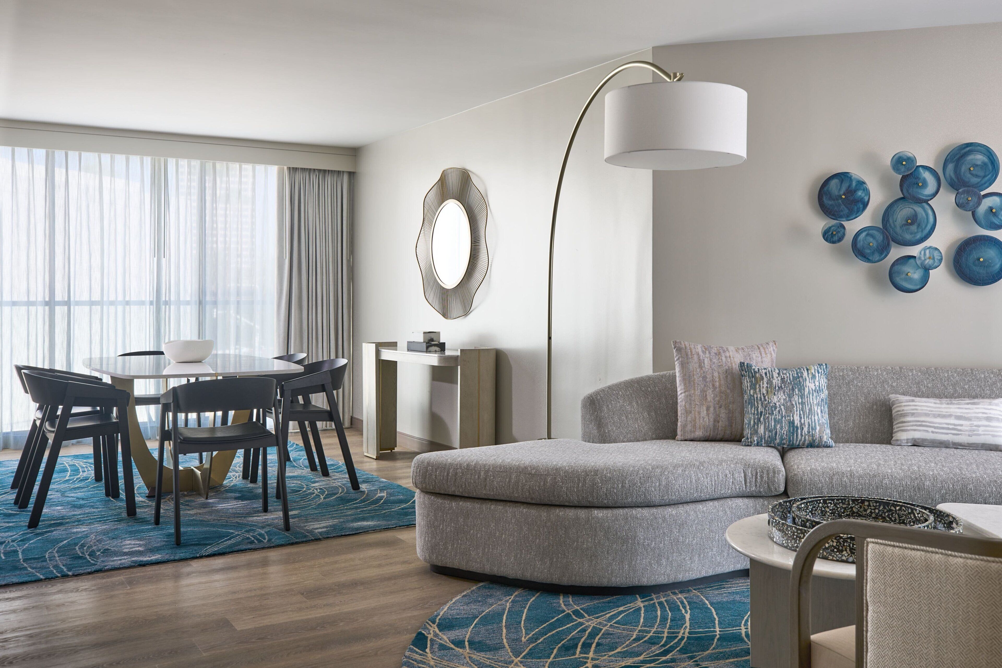 Una sala de estar moderna con un sofá gris, una mesa redonda de centro y una zona de comedor con mesa y sillas.