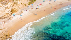 Luchtbeeld van een strand met helder turquoise water, een zandstrand en mensen die van het strand genieten.