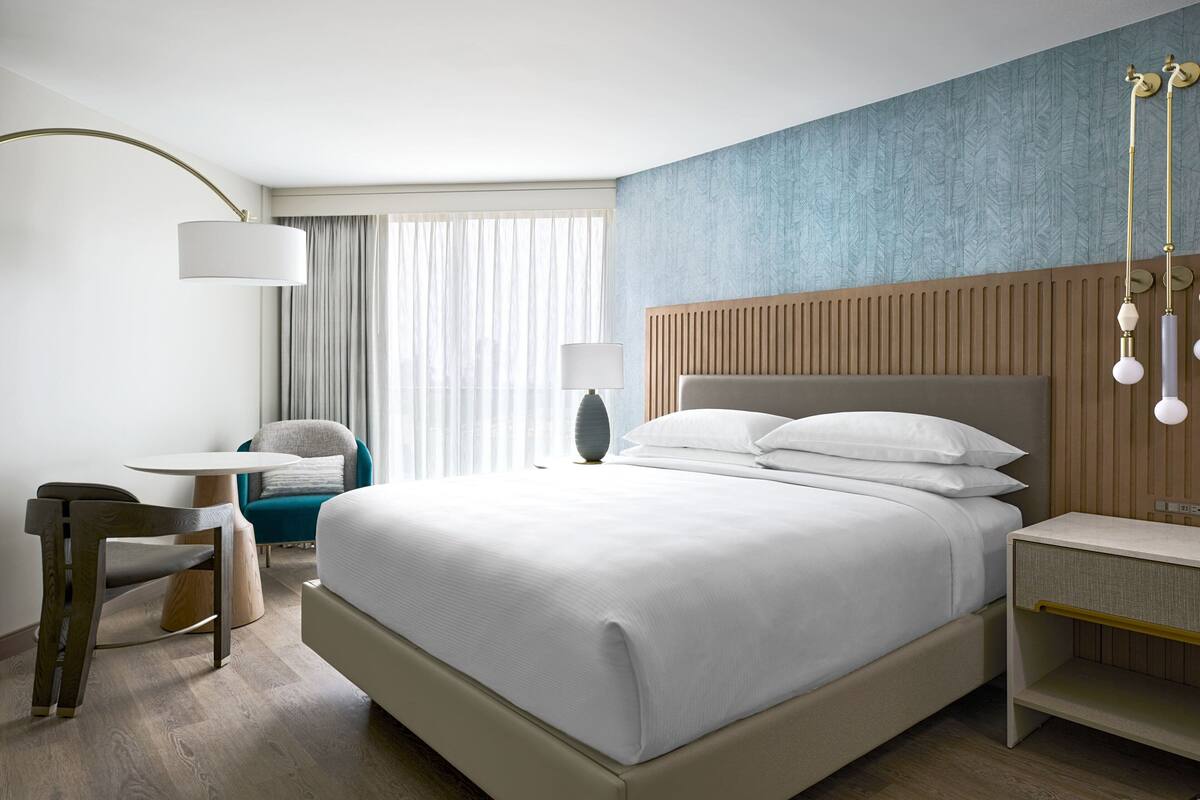 Una habitación de hotel moderna con una cama grande, un escritorio, una silla y un ventanal con cortinas.