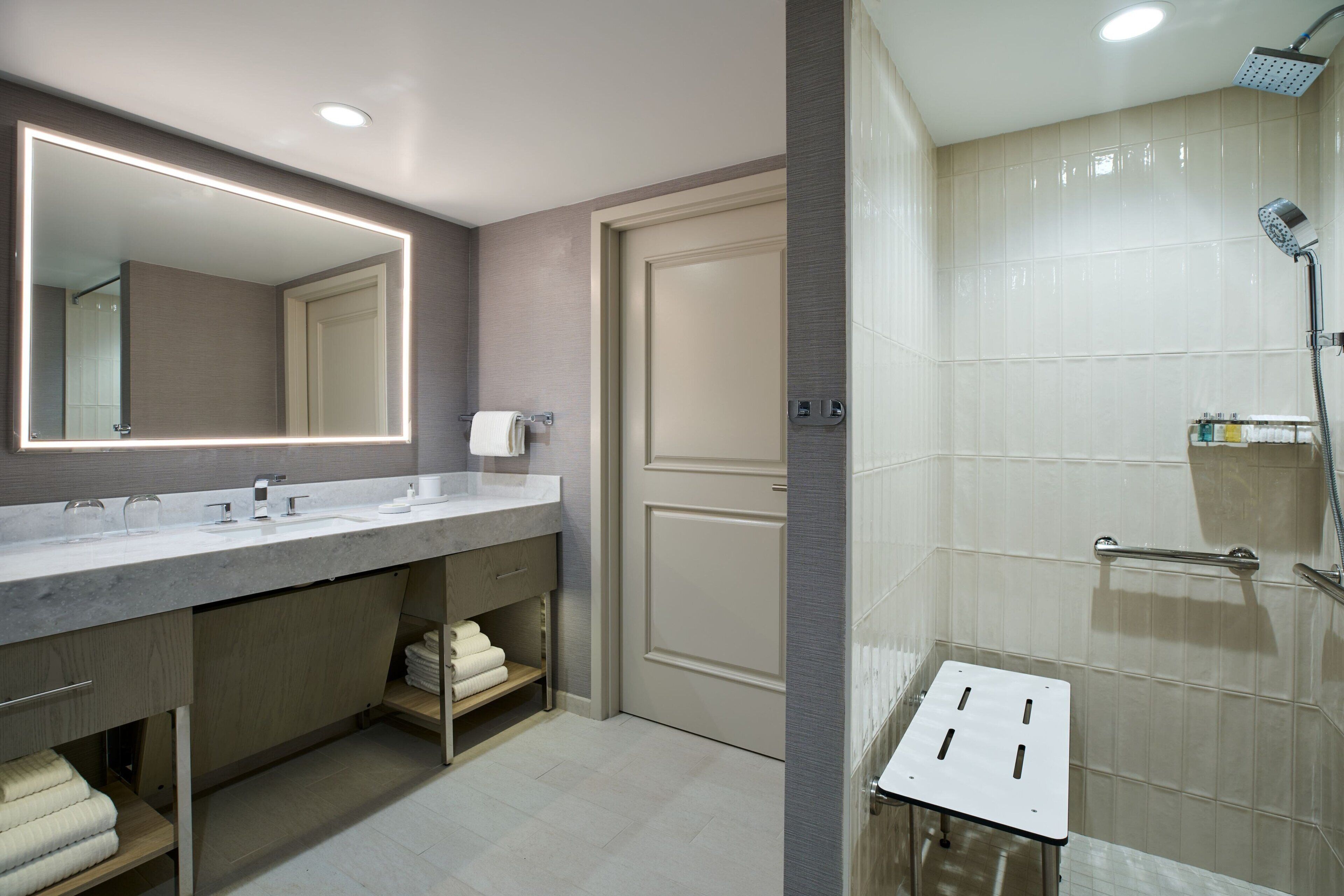 Une salle de bain moderne dotée d’un grand miroir, de deux vasques, d’une douche avec un pommeau de douche amovible et d’un porte-serviettes.
